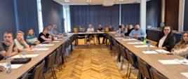 Uczestnicy szkolenia w trakcie wykładu. Na zdjęciu sala konferencyjna, 2 długie stoły ustawione w kształcie litery U. Przy stołach uczestnicy, przed nimi materiały szkoleniowe napoje. Głowy uczestników zwrócone ku wykładowcy