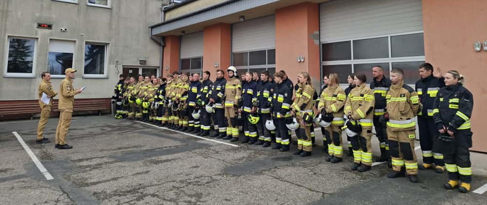 na zdjęciu grupa strażaków – słuchaczy kursu podczas zbiórki przed egzaminem, w tle budynek Komendy