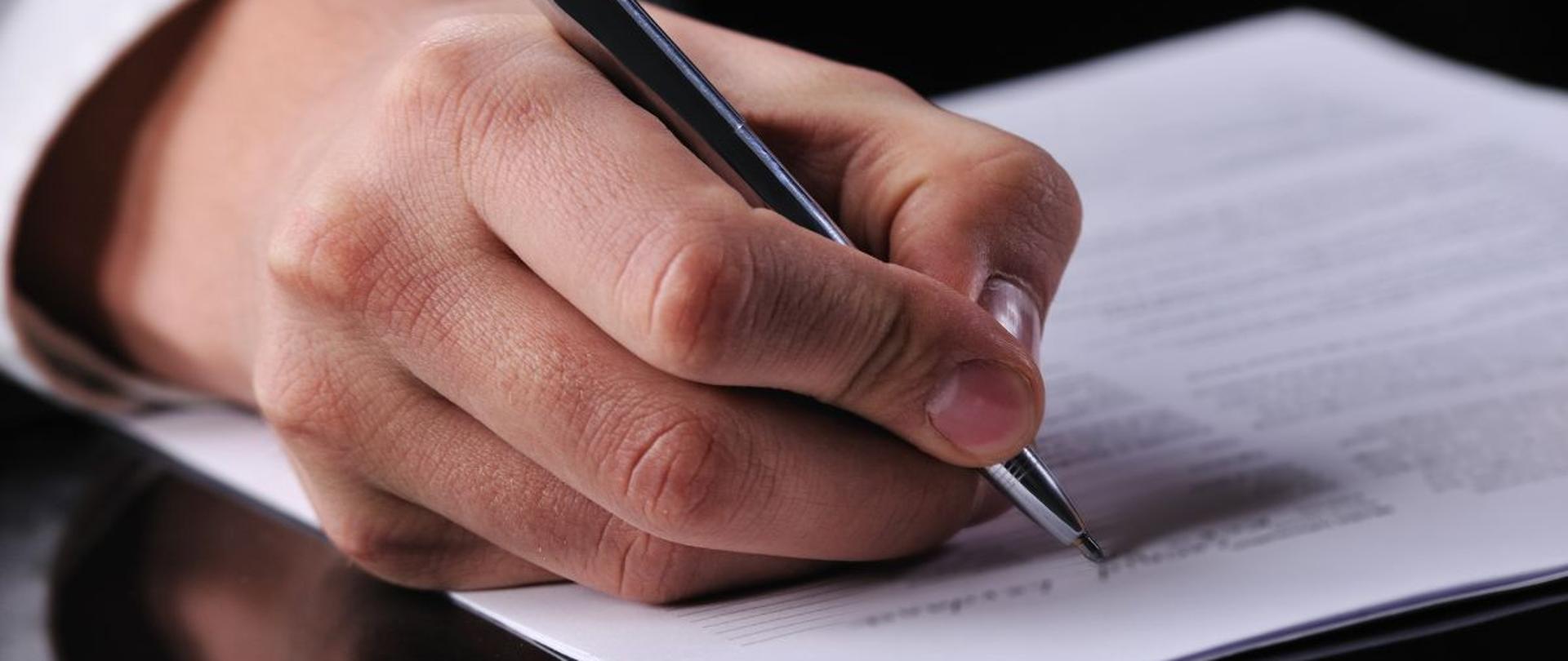 Męska dłoń podpisująca dokument leżący na stole