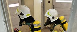 Strażacy w ubraniach specjalnych i hełmach klękają przed drzwiami, 