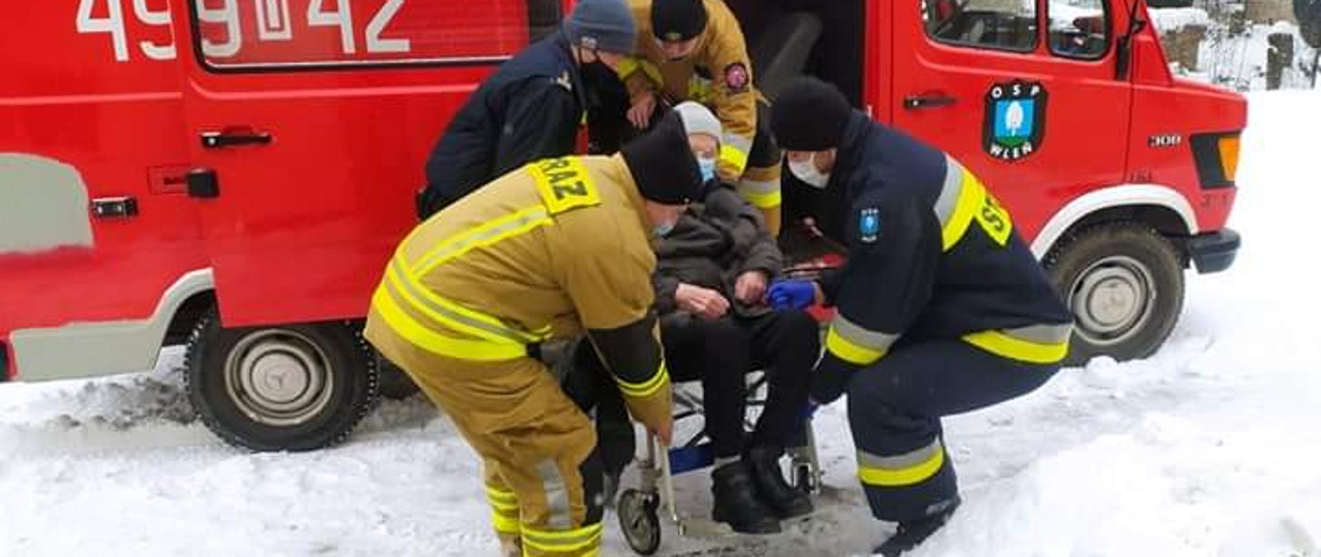 Na zdjęciu strażay pomagaja osobie z niepełnosprawnościa wysiąć z samochodu