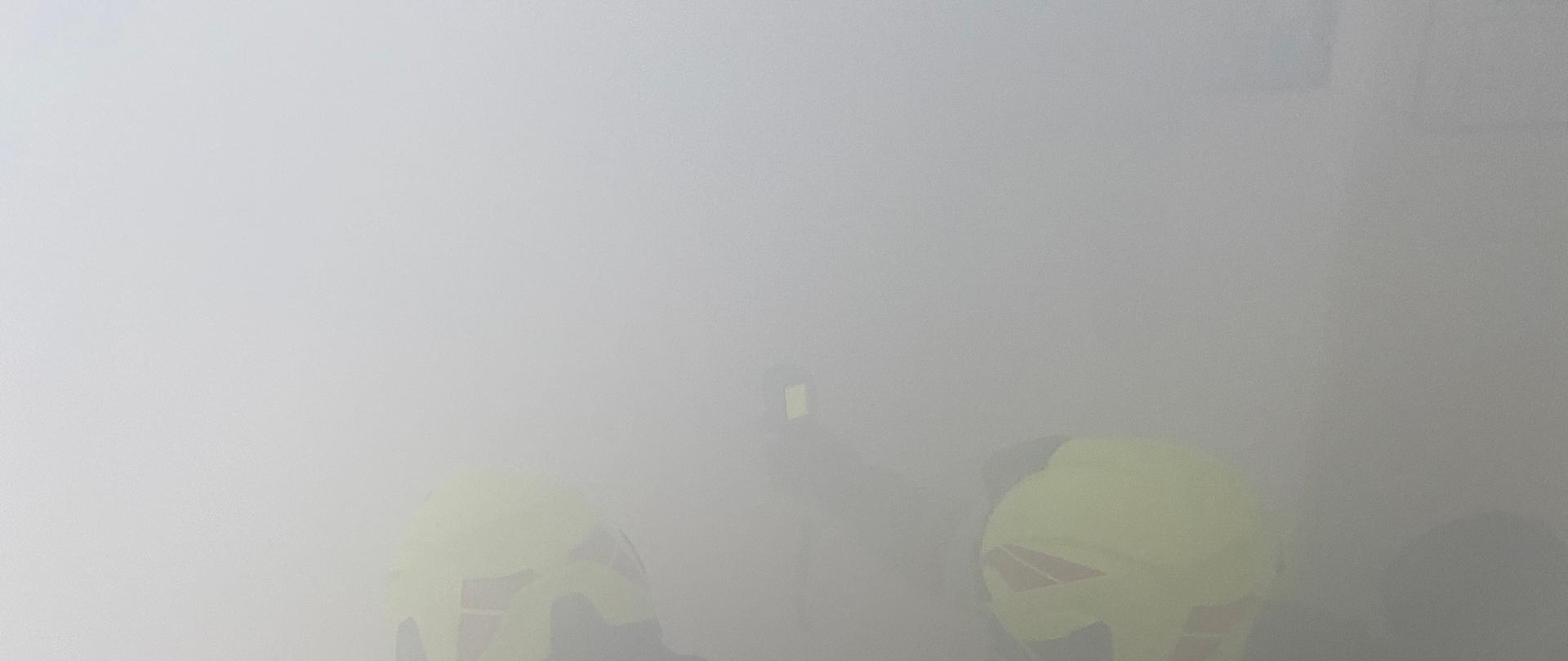 Dwóch ratowników przeszukuje w całkowicie zadymionym pomieszczeniu osób poszkodowanych przy użyciu kamery termowizyjnej