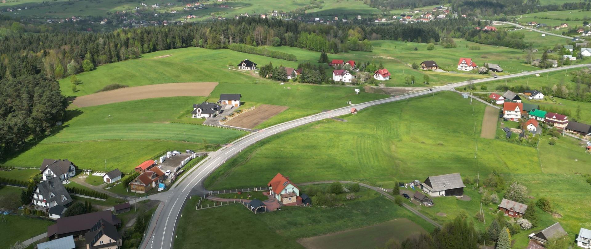 Łuk drogi krajowej nr 28. Widoczna droga dwupasowa na odcinku pomiędzy Kasiną Wielką a Limanową. Wokół zabudowania i domki jednorodzinne. 