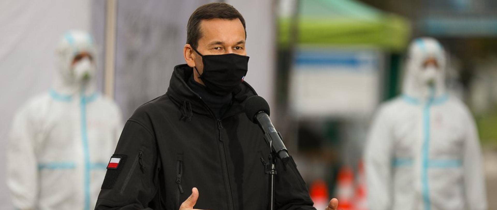 Premier stoi podczas przemówienia, w tle żołnierze WOT w kombinezonach.