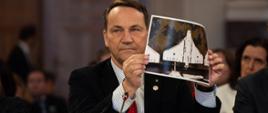 The photo depicts Minister Radosław Sikorski showing a picture of a drone at the 32nd OSCE Ministerial Council meeting