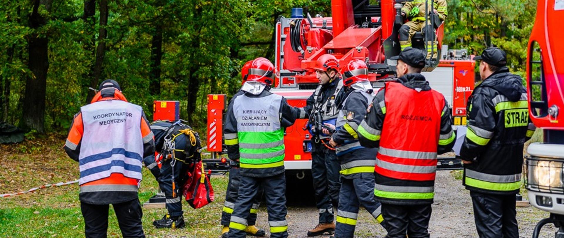 Strażacy konsultują koncepcję działań zdjęcia poszkodowanego paralotniarza z drzewa. 