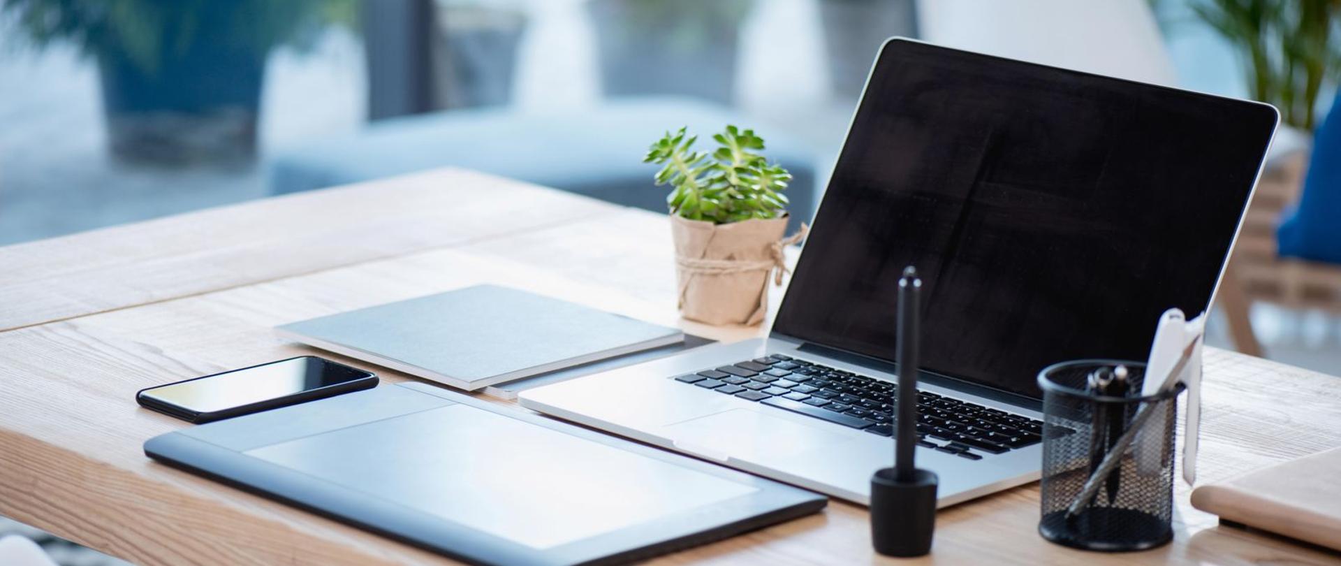 Biurko z laptopem, telefonem i przyborami do pisania.