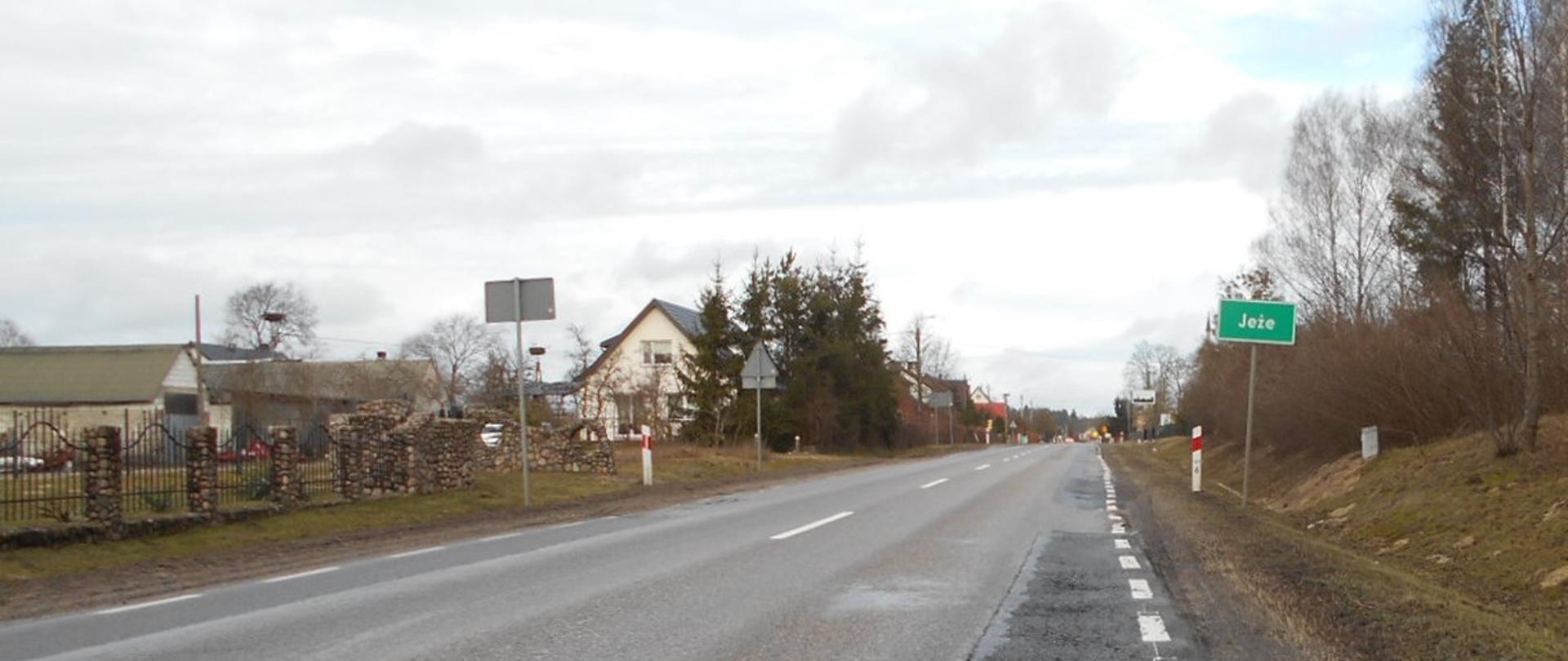 DK63 Borki - Jeże. Wjazd do miejscowości Jeże. Po lewej stronie drogi zabudowania, po prawe znak z nazwą miejscowości.