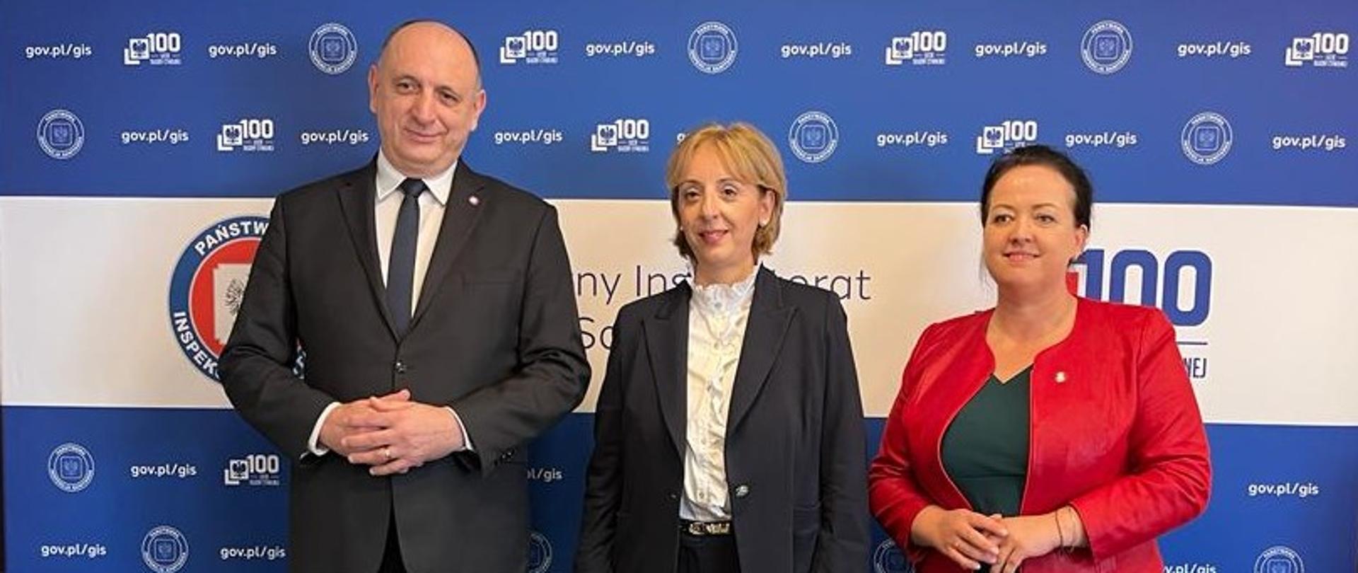 Na tle ścianki GIS stoją: Krzysztof Saczka, Główny Inspektor Sanitarny wz., dr Nino Berdzuli, Dyrektor Biura WHO w Polsce oraz Izabela Kucharska, zastępca Głównego Inspektora Sanitarnego.