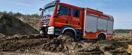 Samochód pożarniczy jedzie po błotnistym terenie.