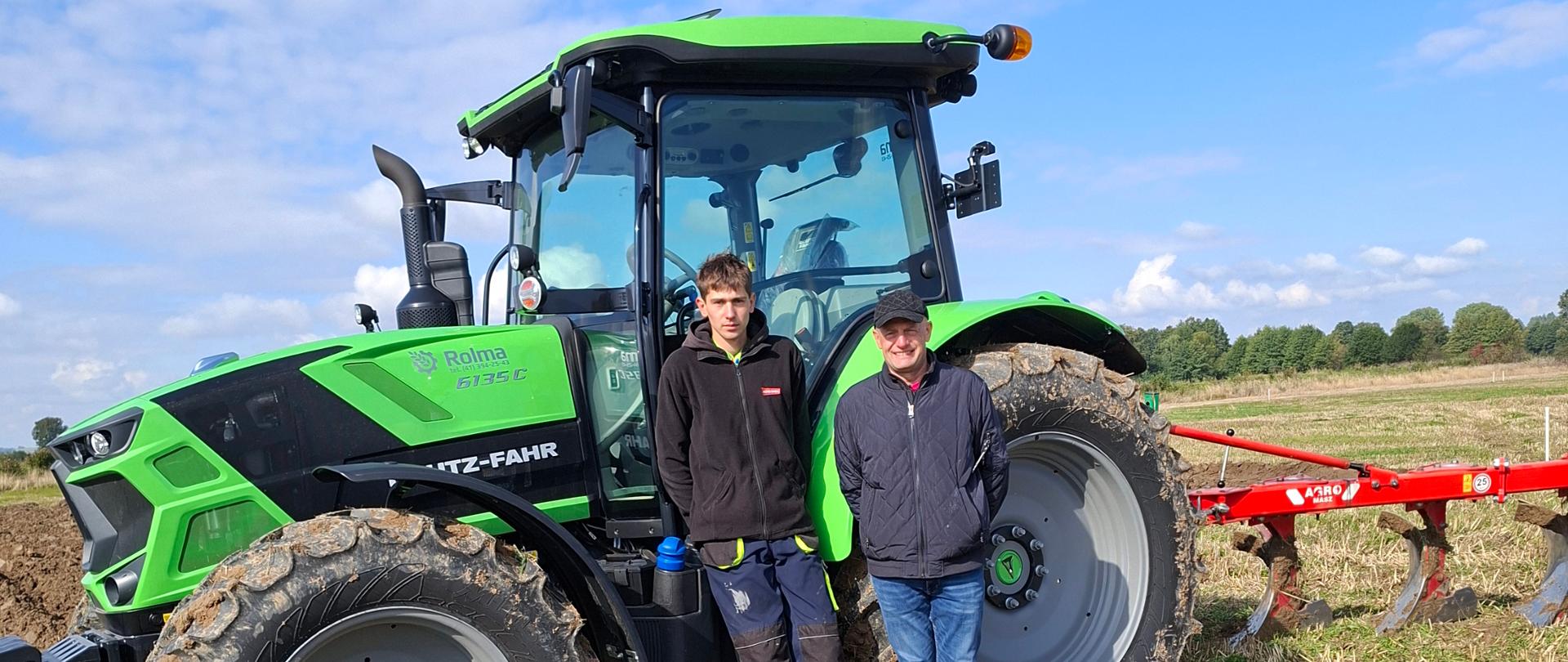 Uczeń wraz z opiekunem na tle ciągnika w trakcie praktycznej części konkursu