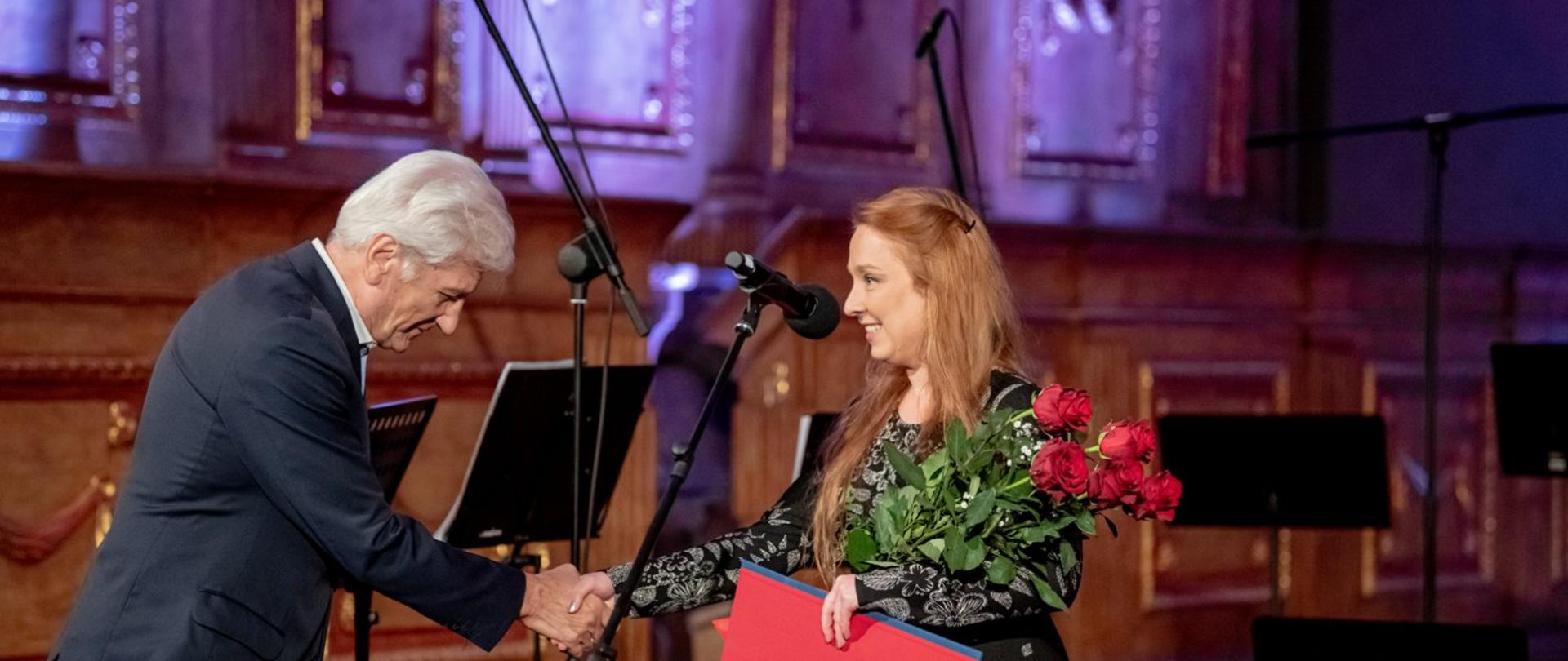 Zdjęcie w poziomie. Mężczyzna gratuluje kobiecie, podaje jej rękę.