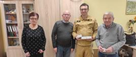 Strażak z czujkami w ręku stojący pomiędzy seniorami 
