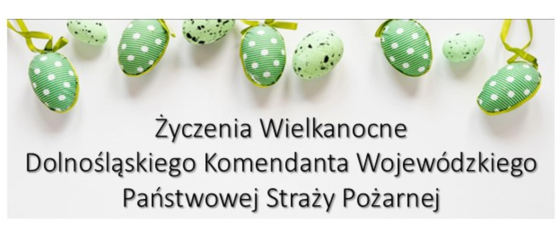 Grafika okolicznościowa na białym tle z czarnym napisem: „Życzenia Wielkanocne Dolnośląskiego Komendanta Wojewódzkiego Państwowej Straży Pożarnej”. W górnej części grafiki, nad tekstem, ułożony jest poziomy rząd zielonych pisanek – część z nich jest gładka w białe kropki z zawiązanymi tasiemkami, a część nakrapiana.