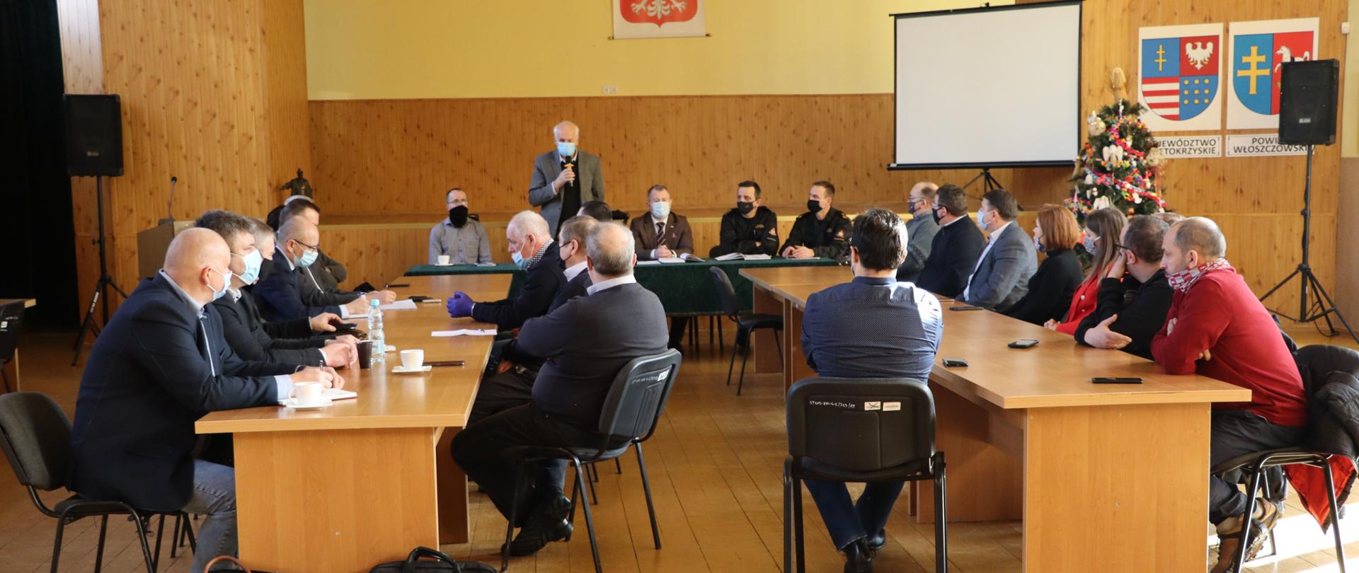 zdjęcie przedstawia salę narad starostwa powiatowego we Włoszczowie. w dwóch rzędach stałów siedzą przedstawiciele zaproszonych instytucji tj. OSP , urzędów gmin , starostwa, powiatowego, w głównejpozycji zdjęcia widać stół prezydialny na którym zasiadają komendant powiatowy PSP we Włoszczowie – st. kpt. Andrzej Pacanowski, Pełnomocnik wojewody świętokrzyskiego ds. realizacji programu szczepień ochronnych przeciwko wirusowi SARS-CoV2 – Jerzy Staszczyk, Wicestarosta – Łukasz Karpiński 