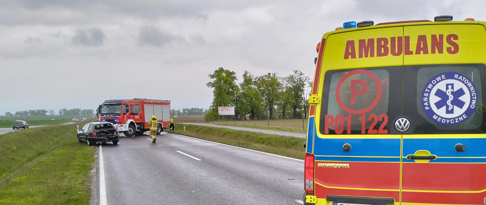 Pojazd pogotowia ratunkowego, a w oddali samochody biorące udział w kolizji oraz samochód straży pożarnej