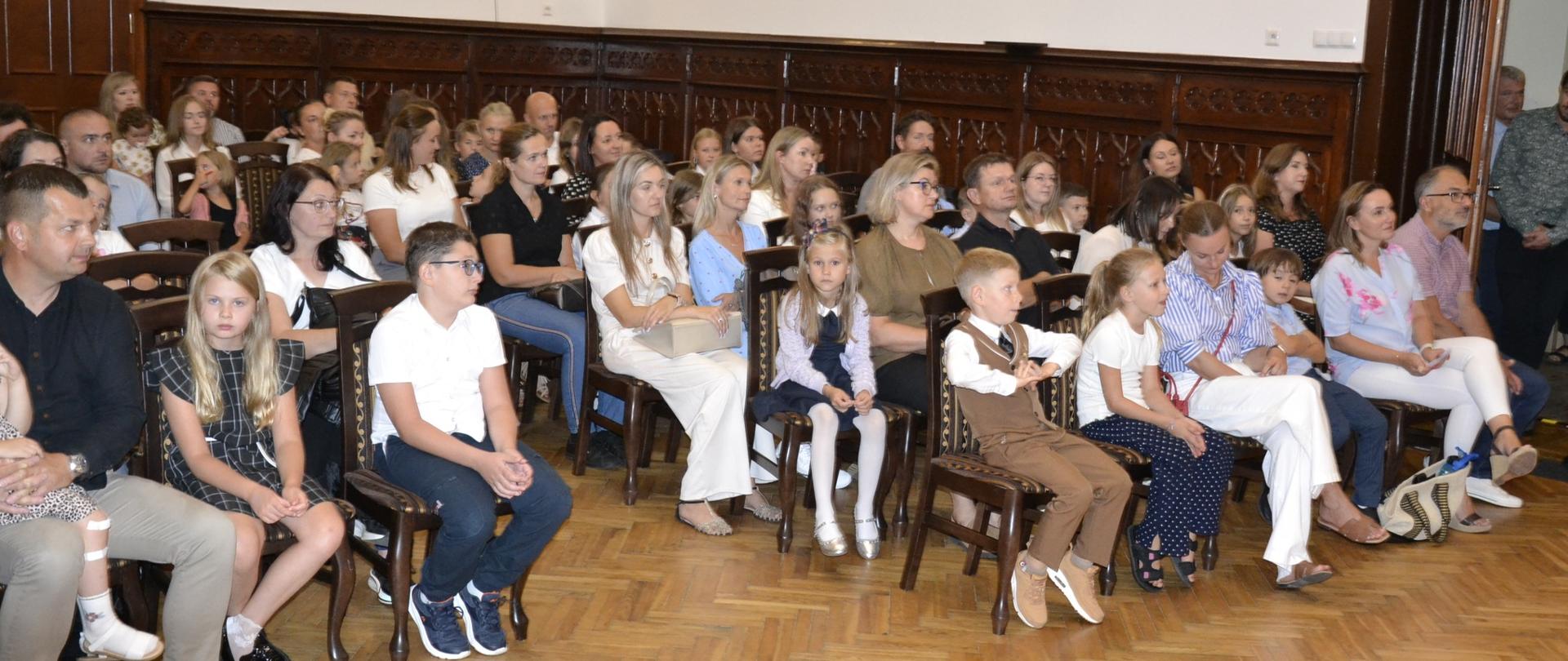 Grupa dzieci i rodziców siedzi w Sali Królewskiej podczas uroczystego powitania uczniów klas pierwszych Państwowej Szkoły Muzycznej w Mielcu, 1 września 2025 roku