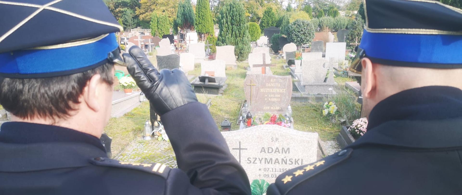 Zdjęcie przedstawia strażaków oddających honor nad grobem