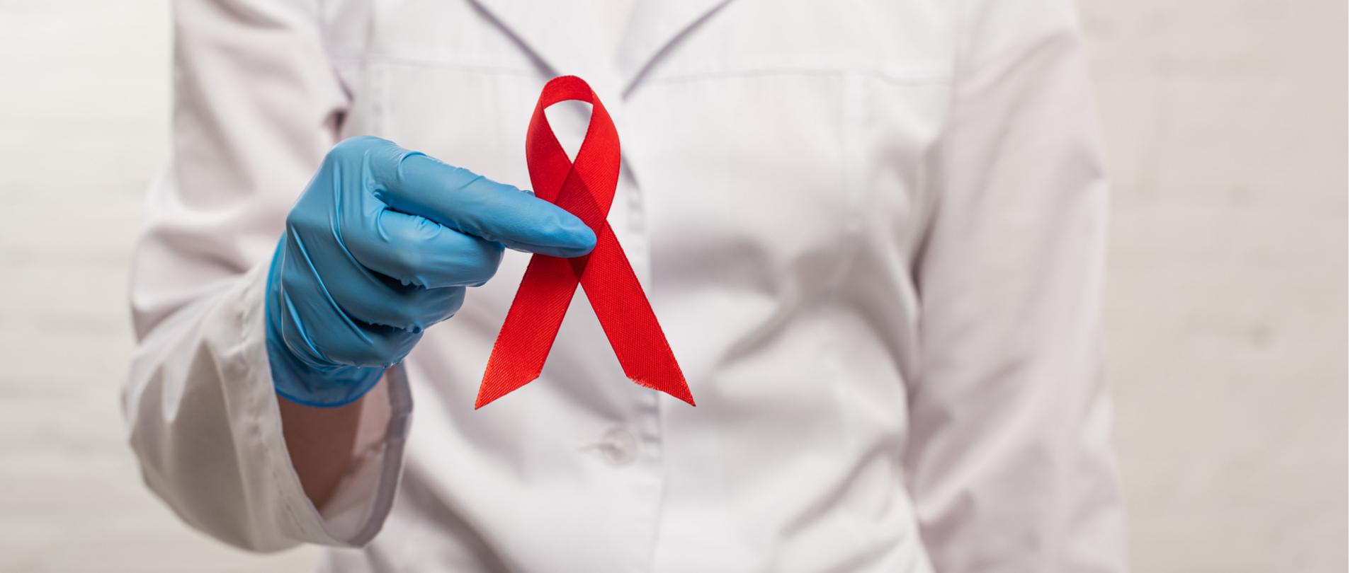 Na zdjęciu jest lekarz trzymający w dłoni czerwoną wstążkę.