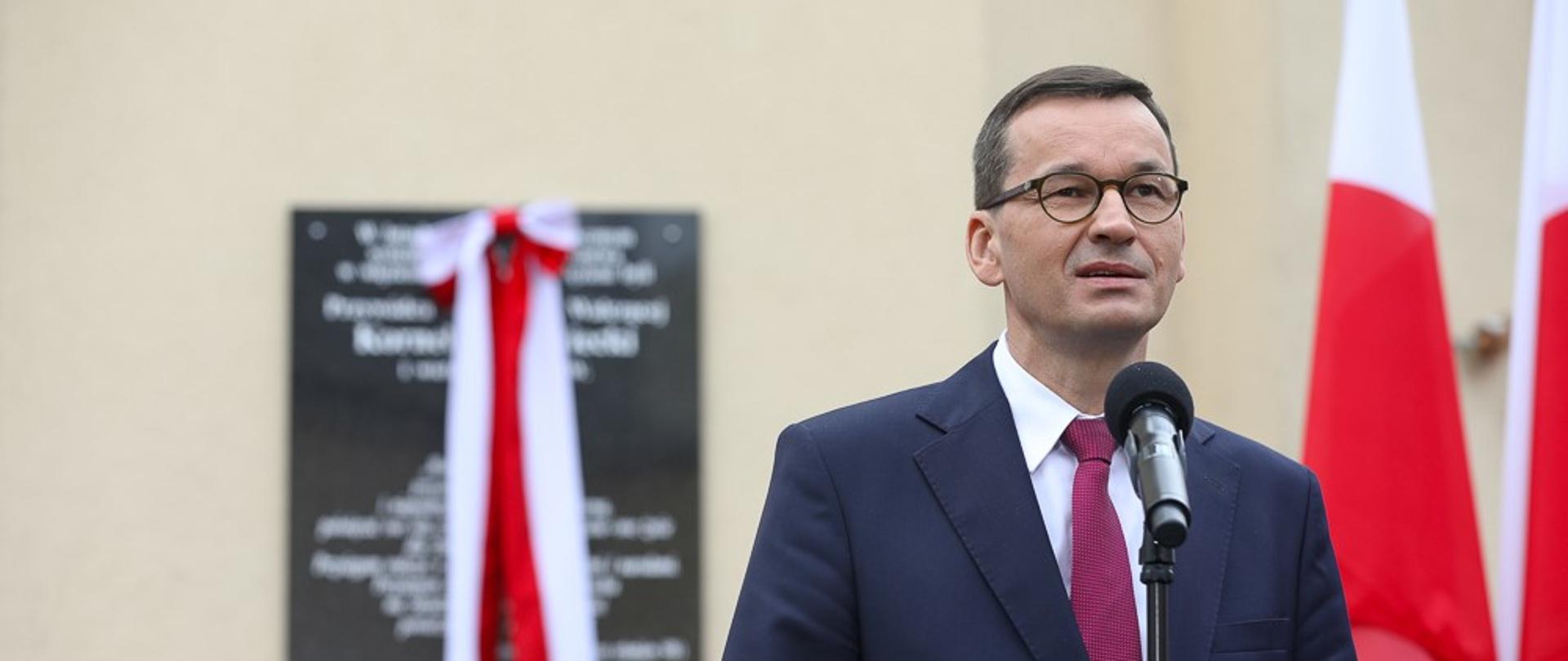 Premier Mateusz Morawiecki przemawia na tle odsłanianej tablicy.
