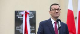 Premier Mateusz Morawiecki przemawia na tle odsłanianej tablicy.