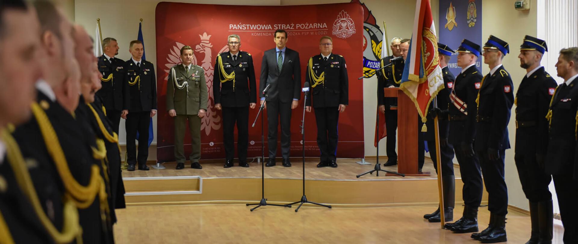 Na zdjęciu strażacy podczas uroczystej zbiórki z okazji Narodowego Święta Niepodległości w Komendzie Wojewódzkiej PSP w Łodzi. Po lewej stronie pododdział odznaczonych. W środku kadru kierownictwo PSP. Po prawej poczet sztandarowy Komendy Wojewódzkiej PSP w Łodzi.