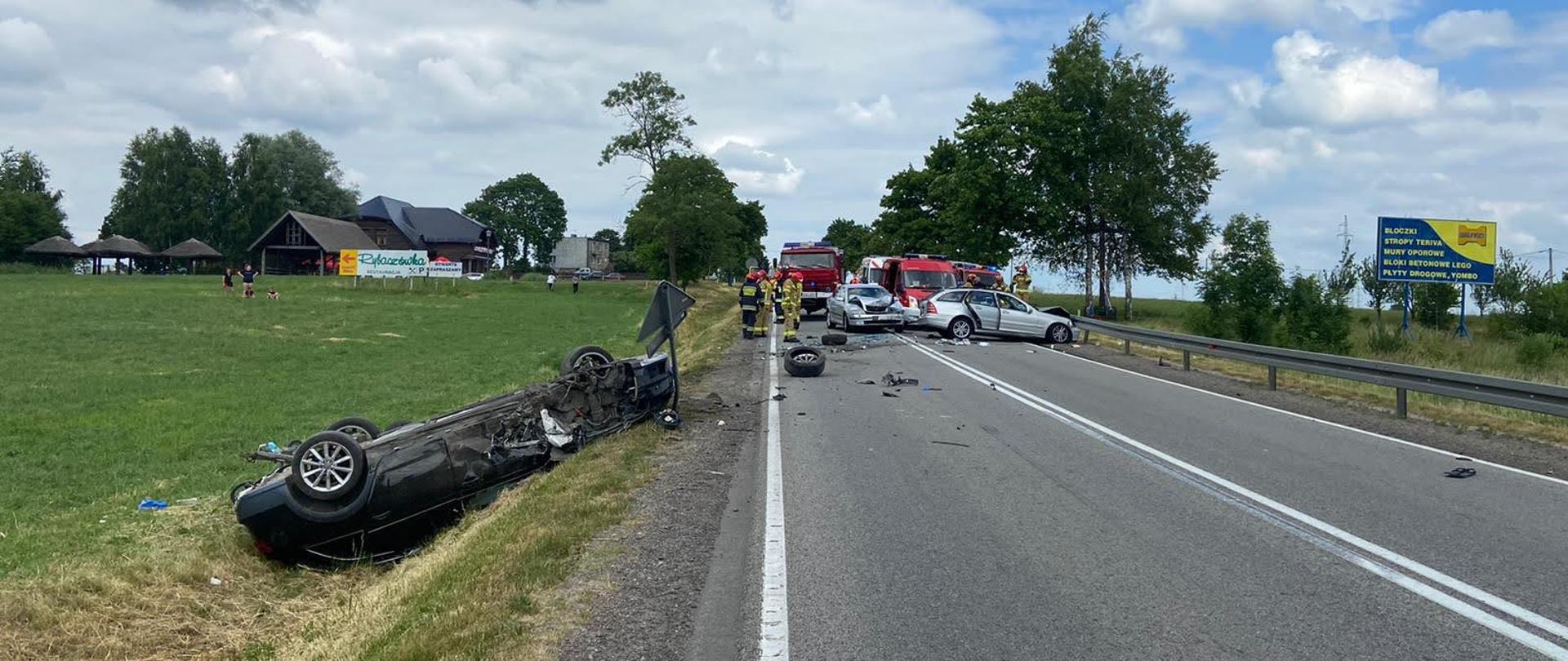 Teren działań w tle uszkodzone pojazdy i wozy strażackie.