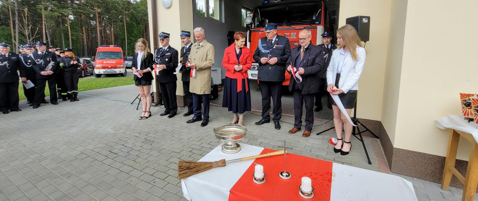 Uczestniczy uroczystości zgromadzeni na planu przed remizą. W tle nowa remiza.