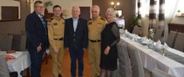 Dzień Strażaka emerytów pożarnictwa. W sali restauracyjnej do wspólnego zdjęcia pozują: komendant i zastępca komendanta powiatowego PSP oraz zarząd koła emerytów. Strażacy ubrani są w mundury służbowe koloru piaskowego. 