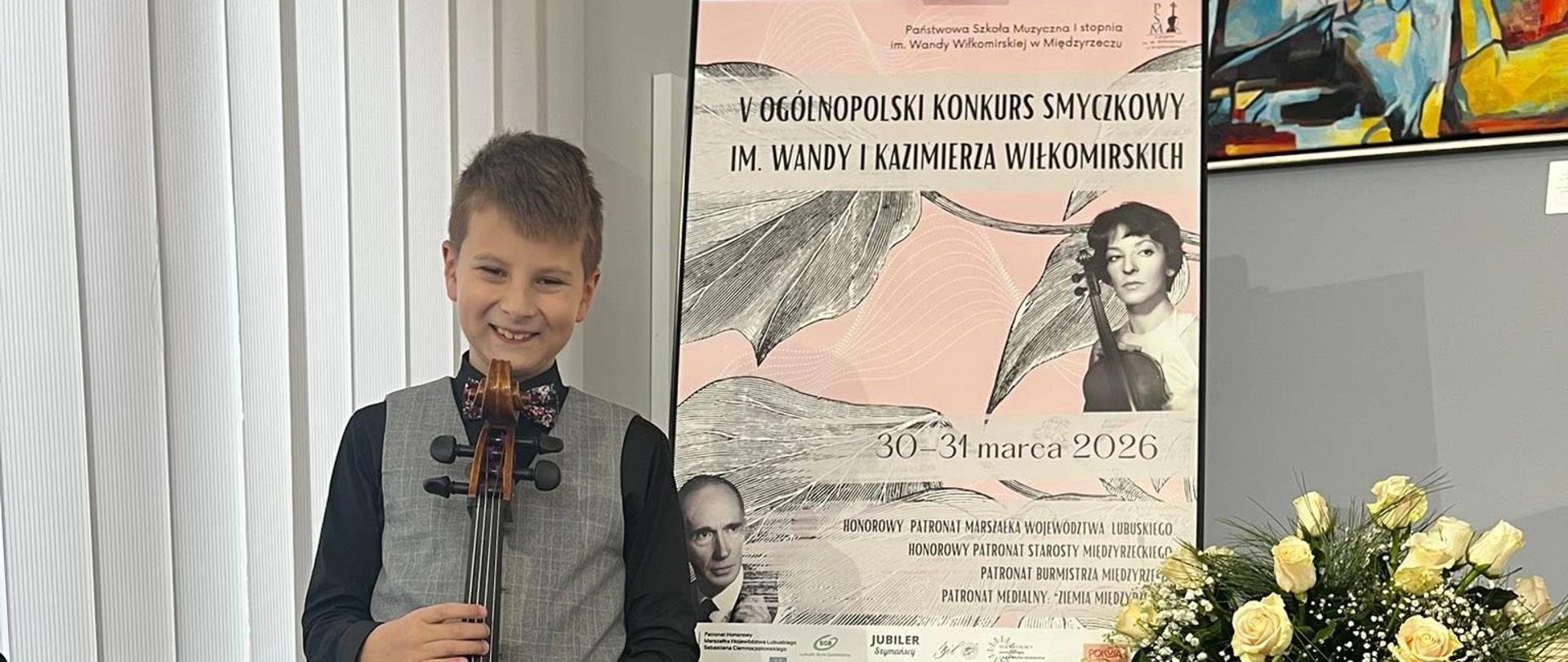 Uczeń w galowym stroju trzymający wiolonczelę, z prawej strony baner reklamujący Konkurs smyczkowy w Międzyrzeczu. 