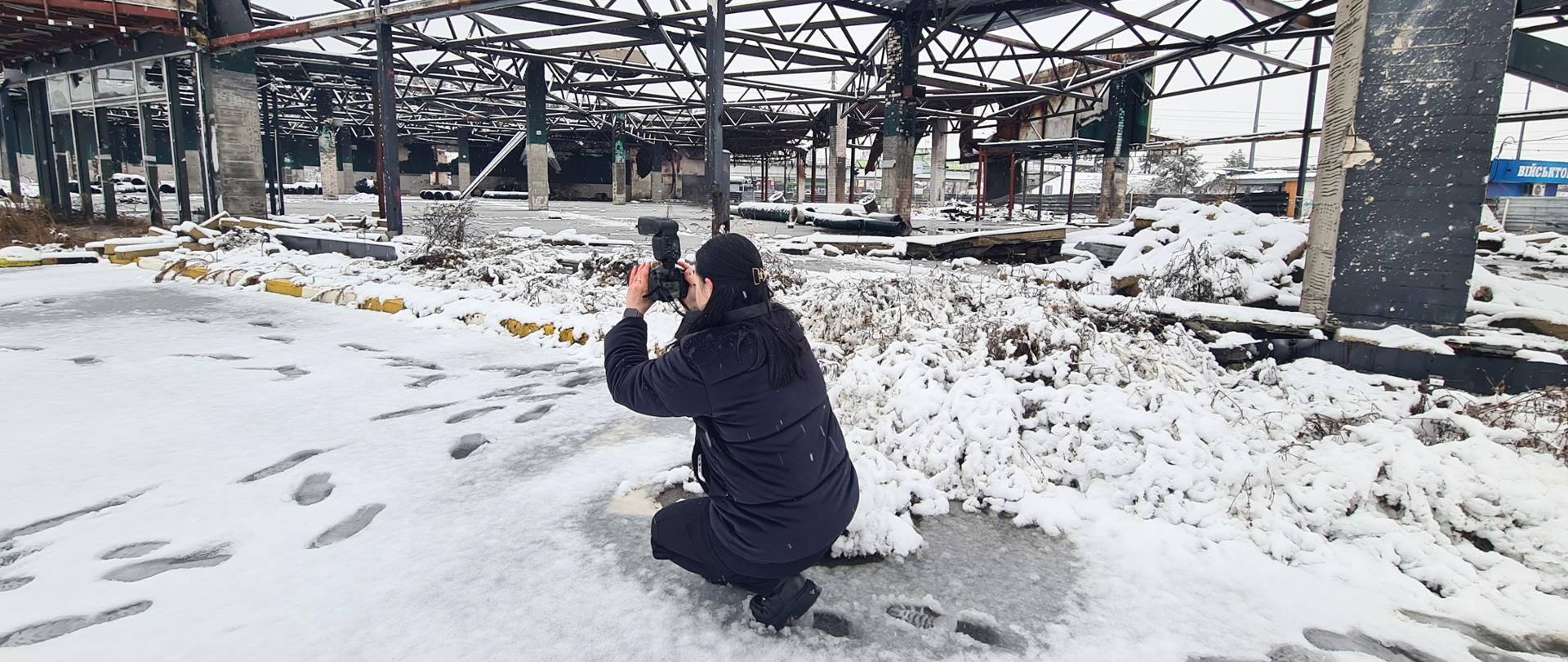 Fotografia przedstawia funkcjonariuszkę Narodowej Policji Ukrainy dokumentującej zniszczenia wojenne za pomocą aparatu fotograficznego w trakcie szkolenia.