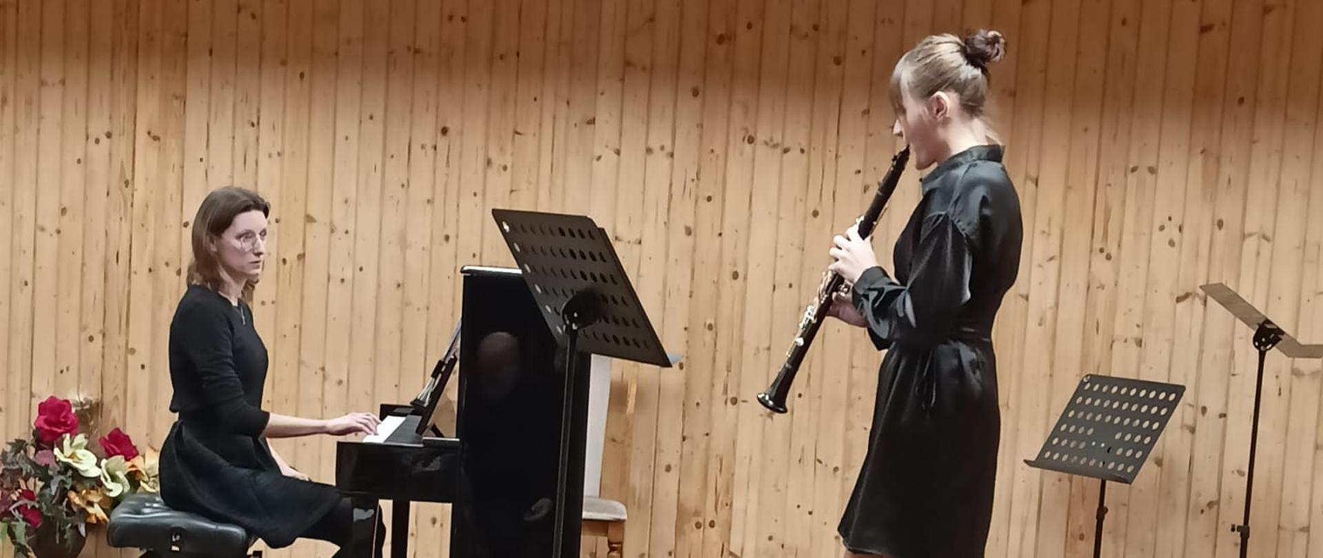 Nastolatka gra na klarnecie, po lewej stronie kobieta gra na pianinie.