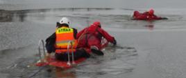 Zdjęcie przedstawia dwóch odpowiednio zabezpieczonych ratowników PSP na saniach wodno-lodowych śpieszących z pomocą osobie, pod którą załamała się tafla lodu
