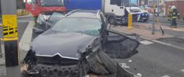Uszkodzony samochód osobowy za nim uszkodzona ciężarówka blokujące skrzyżowanie.
