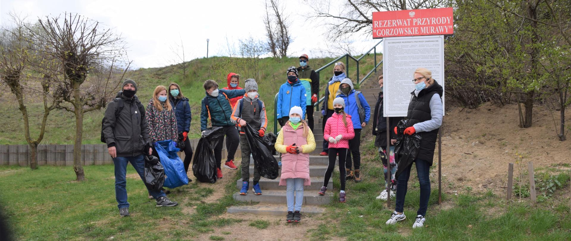 Na zdjęciu uczestnicy sprzątania rezerwatu. Ustawieni na schodach przed wejściem do rezerwatu przyrody. Obok tablica z nazwą rezerwatu 