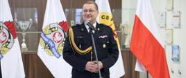 Odchodzący na emeryturę Zastępca Komendanta Centralnej Szkoły PSP przemawiający do mikrofonu, w tle flagi stojące na stojakach