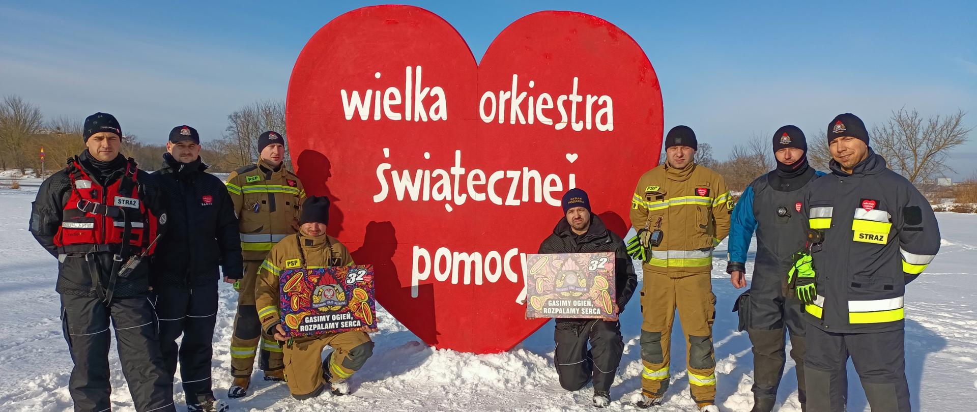 strażacy stoją przy dużym sercu WOŚP