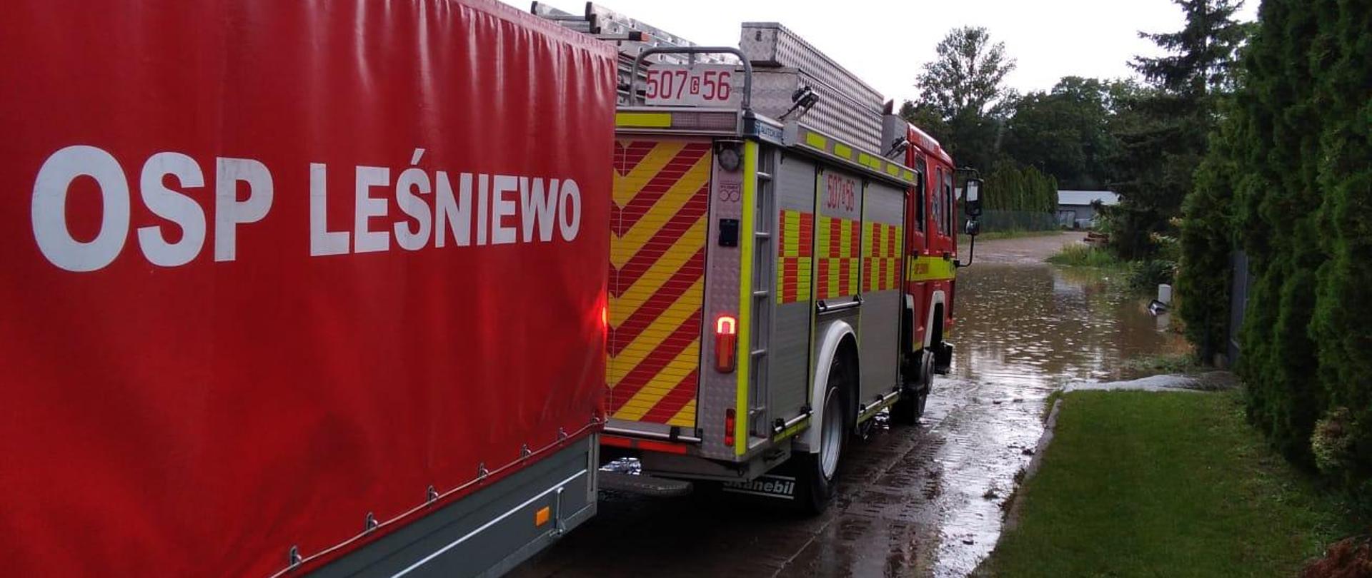 Na pierwszym planie zastęp z OSP Leśniewo oraz przyczepa do przewożenia zestawu pompowego. Na drugim planie ulica Tulipanowa w Kosakowie.