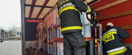Strażacy za pomocą pasów mocują kosze w których transportowane są butle tlenowe do podłoża ładowni samochodu ciężarowego zabezpieczają je przed przemieszczeniem w czasie transportu.