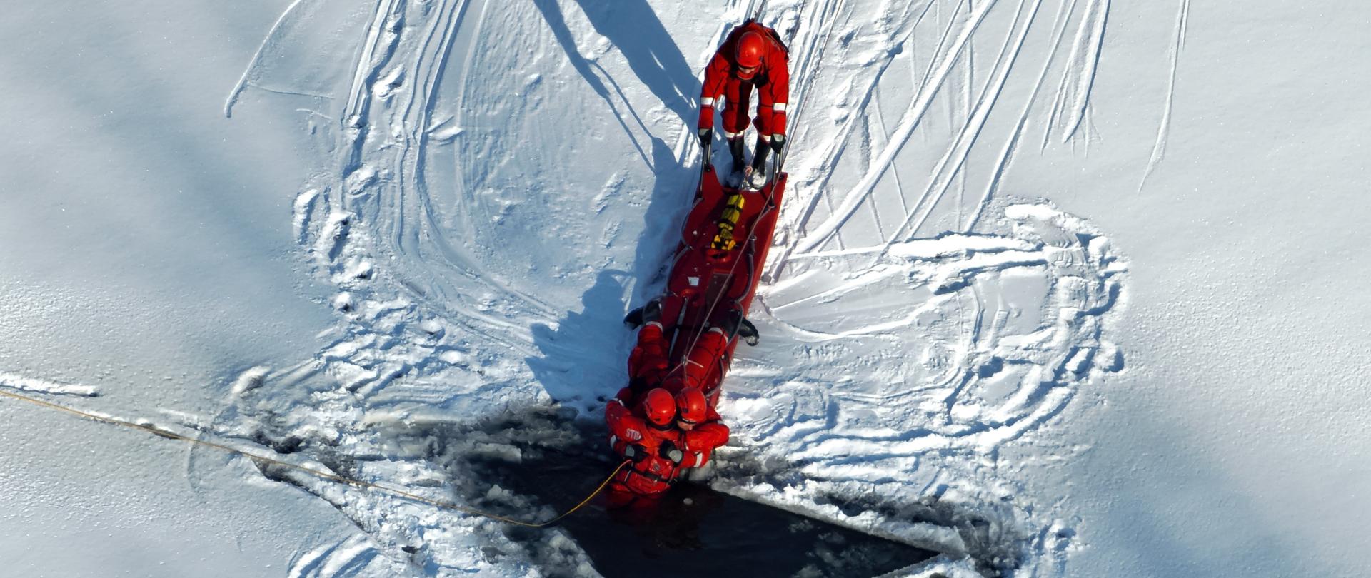Na zdjęciu widzimy ćwiczących strażaków, wykonujących działania na lodzie przy użyciu sani lodowych.
