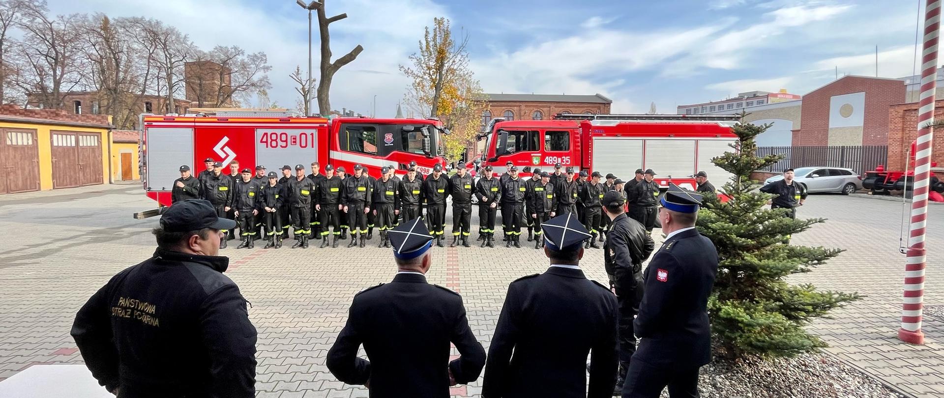 Na pierwszym planie funkcjonariusze KP PSP w Pabianicach oraz Zarząd OP ZOSP RP w Pabianicach. Na drugim planie ustawieni przed samochodami OSP Dłutów i OSP Lutomiersk absolwenci szkolenia podstawowego dla strażaków ratowników OSP.