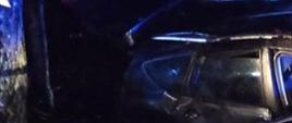 Zdjęcie wykonane w nocy. Widać na nim pojazd osobowy który nosi ślady dachowania. Auto zniszczone z każdej strony. Zdjęcie oświetlone niebieskimi lampami błyskowymi