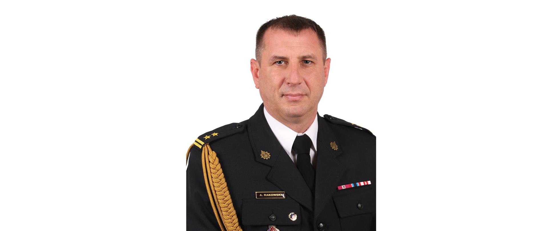 Mężczyzna, ciemny blondyn, lekko uśmiechnięty w białej koszuli z krawatem i granatowej marynarce munduru, ze złotymi dystynkcjami.