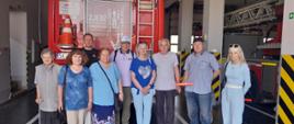 Zdjęcie przedstawia strażaka z słuchaczami Uniwersytetu Trzeciego Wieku na tle wozu pożarniczego