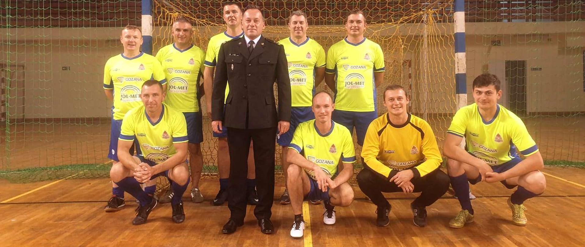 Zawodnicy wraz z Komendantem stoją na tle bramki na płycie boiska.
