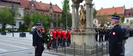 Zdjęcie przedstawia strażaków składających wiązankę pod pomnikiem św. Floriana w Myślenicach