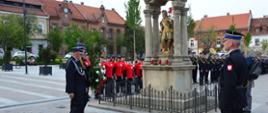 Zdjęcie przedstawia strażaków składających wiązankę pod pomnikiem św. Floriana w Myślenicach
