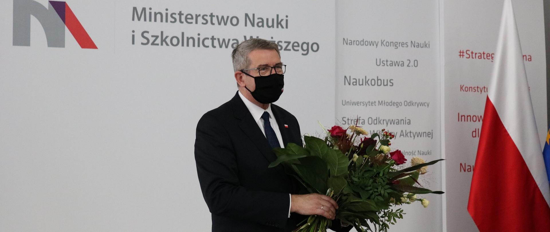Minister stoi z bukietem kwiatów.