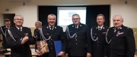 Na zdjęciu stoją druhowie Ochotniczych Straży Pożarnych ubrani w mundury galowe. Zdjęcie wykonane w budynku ośrodka kultury.