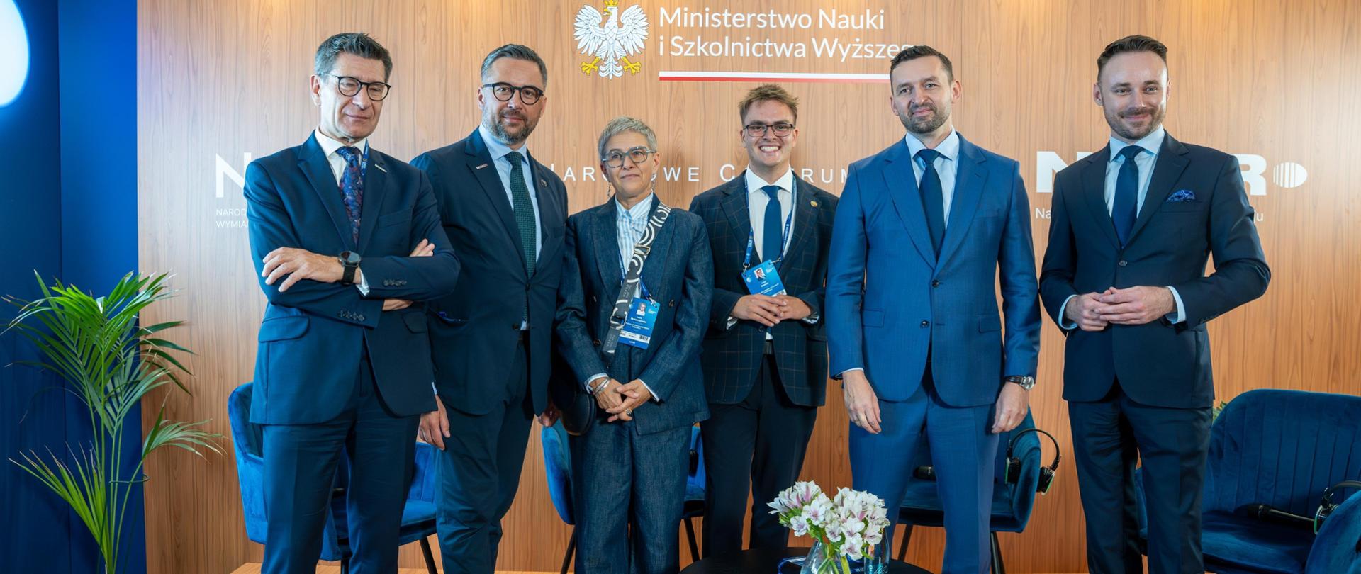 Pamiątkowe zdjęcie uczestników Forum w strefie Ministerstwa Nauki i Szkolnictwa Wyższego podczas Forum Ekonomicznego w Karpaczu. Grupa stoi na scenie przygotowanej do debat i rozmów eksperckich. Wśród stojących jest Minister Marcin Kulasek i Wiceminister Maria Mrówczyńska.
